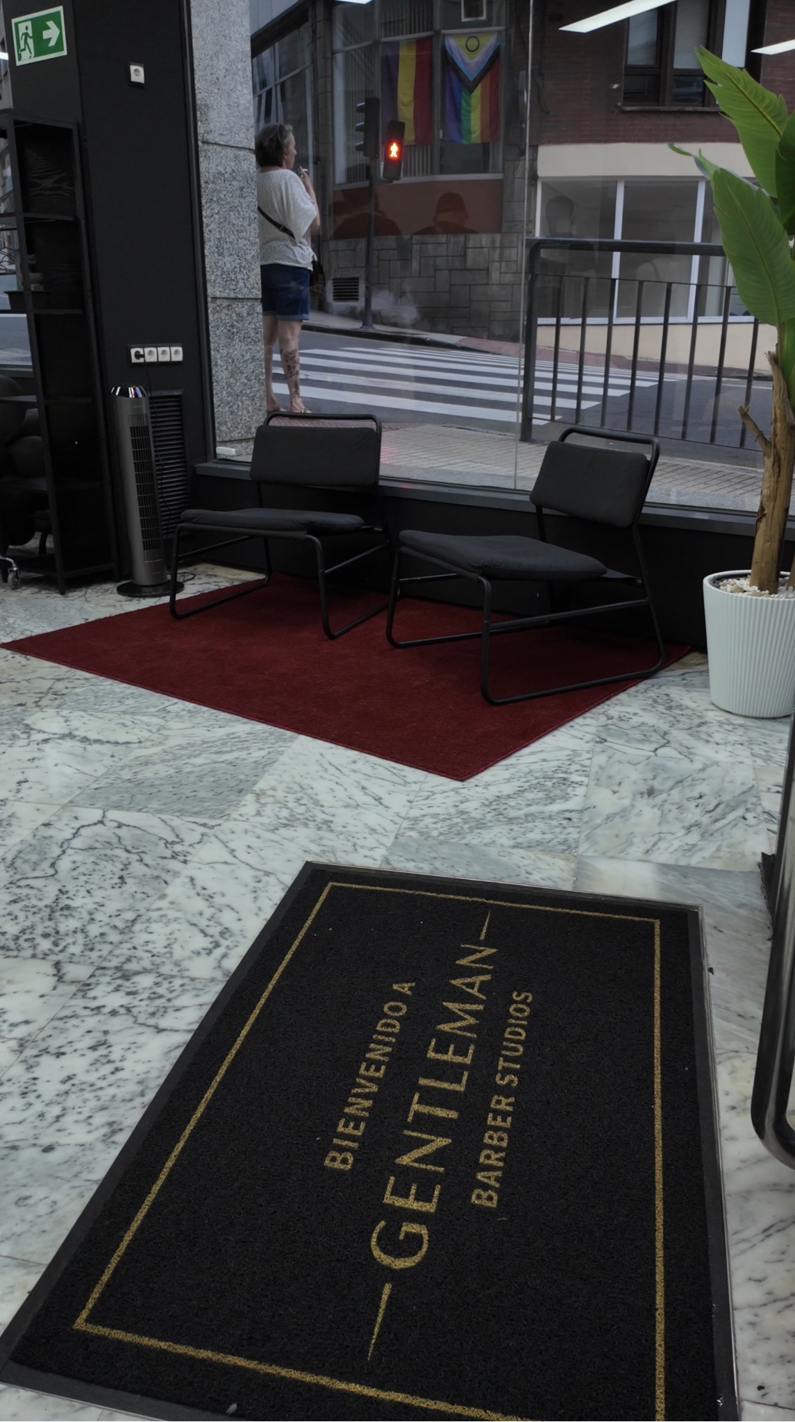 Interior con celpudo de Gentleman Barber Studios con rótulo en tonos negros y dorados y con sillones negros sobre alfombra roja